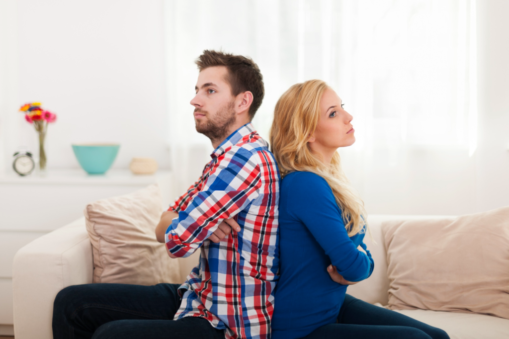 A frustrated couple sitting back to back on a couch, arms crossed, showing tension and emotional distance during a relationship conflict. Divorcing Covert Narcissist